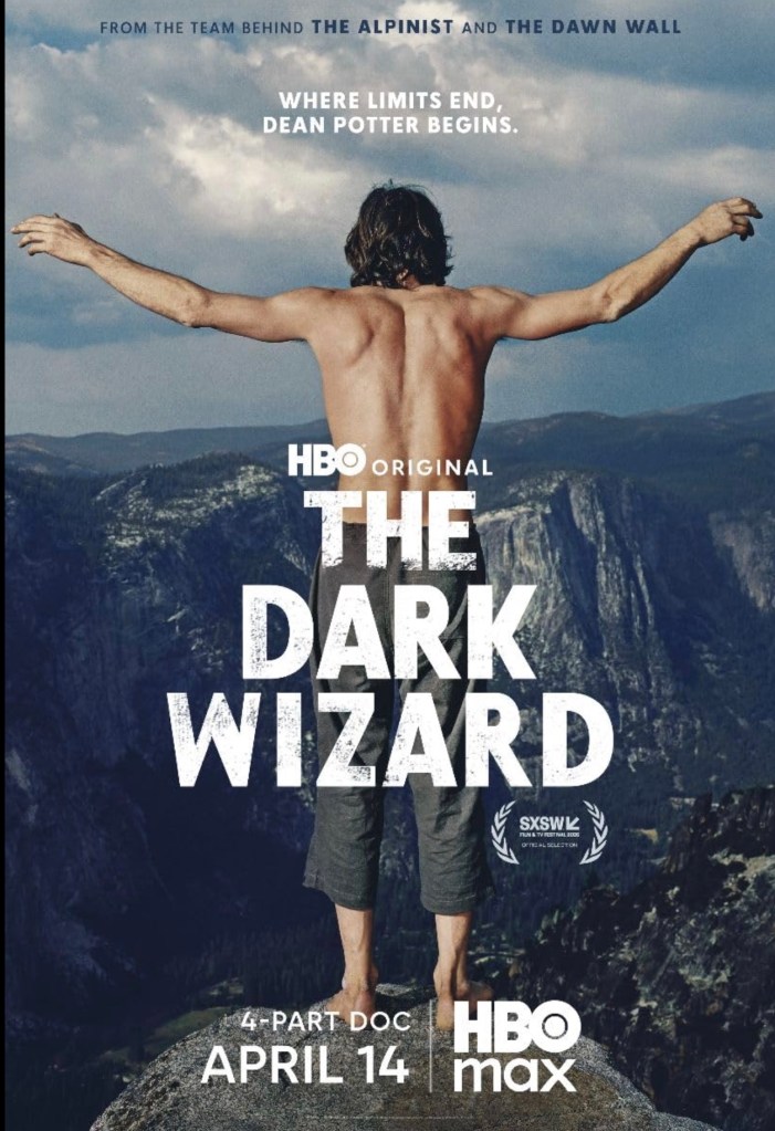 A shirtless man standing with his arms outstretched on a cliff, overlooking a vast mountainous landscape, promoting the HBO documentary 'The Dark Wizard'.